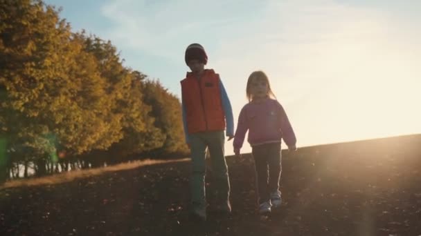 Хлопчик і дівчинка виходять на вулицю на заході сонця — стокове відео