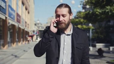 Sakallı adam şehrin sokak yürüyor ve telefonla konuşmak