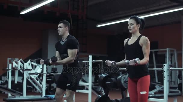 Joven hombre y mujer levantando pesas en un gimnasio — Vídeo de stock