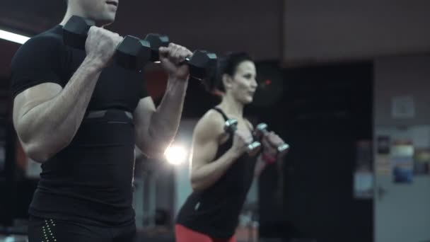 Joven hombre y mujer levantando pesas en un gimnasio — Vídeos de Stock