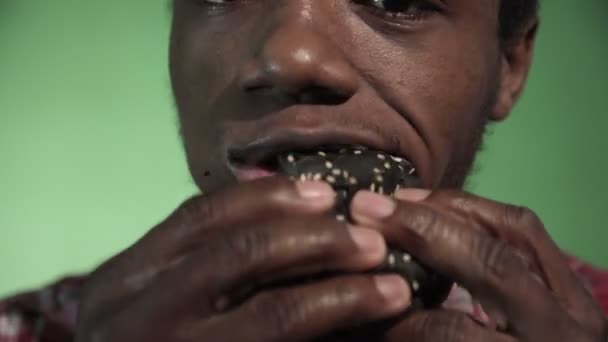 Close shot African man eating black burger — Stock Video