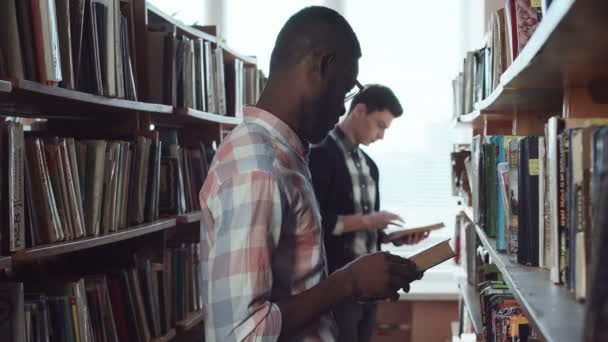 Mannelijke studenten op zoek naar boeken in bibliotheek — Stockvideo