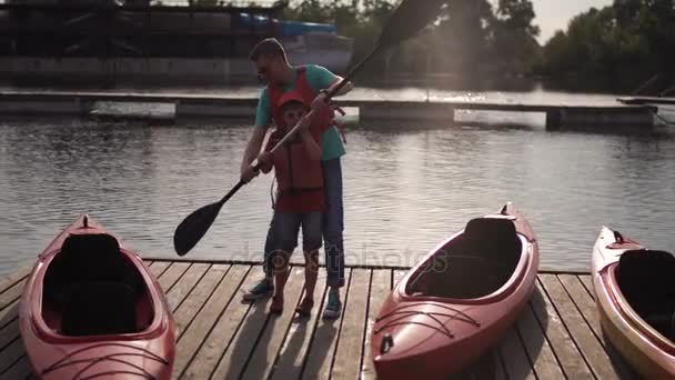 El padre enseña al hijo cómo usar un remo en un kayak. — Vídeos de Stock