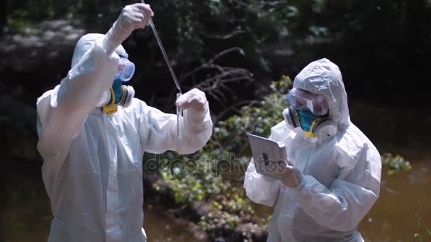 Двоє екологічних працівників у біогазових костюмах відбирають воду — стокове відео