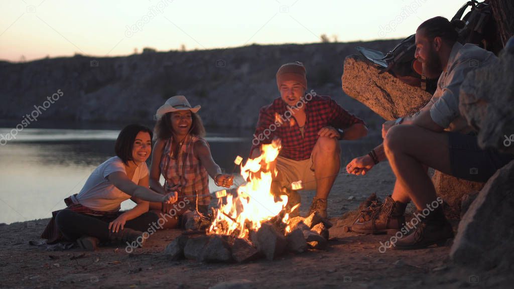 Cheerful friends relaxing around campfire
