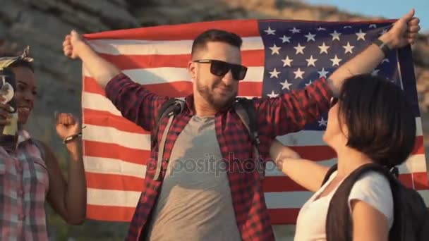 Excited friends posing among rocks with flag — Stock Video