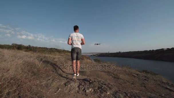 Чоловік контролює безпілотник на березі річки — стокове відео