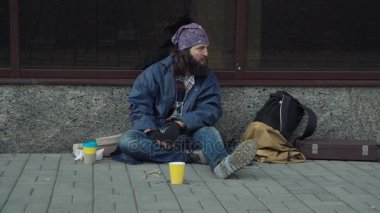 Sarhoş bir evsiz adam sokakta oturuyor.