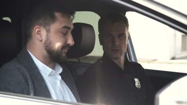 Oficial de policía sentado en el coche con el hombre detenido — Vídeos de Stock