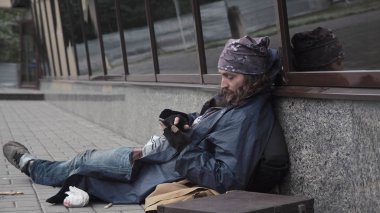 Smartphone ile sokakta oturan dilenci adam sakallı.