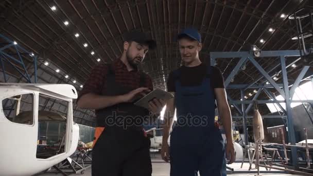 Twee mannen in vliegtuigen hangar bespreken — Stockvideo