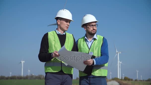 Dos ingenieros discutiendo contra parque eólico — Vídeo de stock