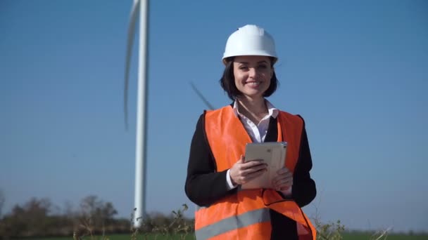 Усміхнена жінка-інженер, що стоїть проти вітроелектростанції — стокове відео