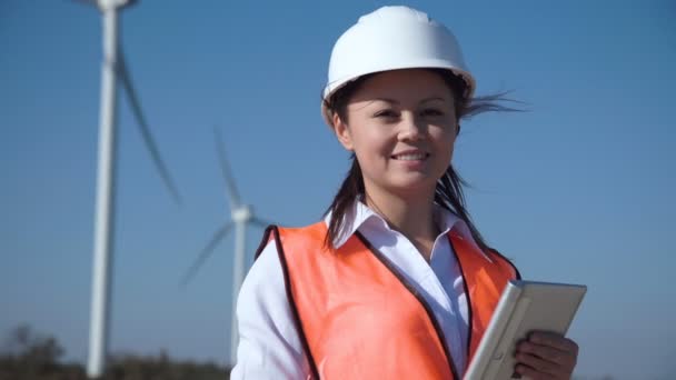 Une ingénieure souriante debout contre un parc éolien — Video