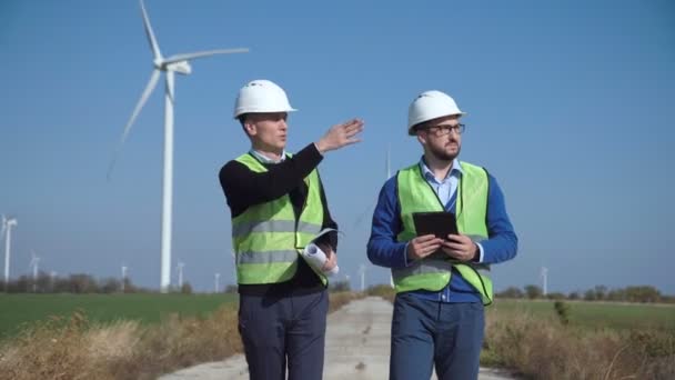 Dois engenheiros discutindo contra o parque eólico — Vídeo de Stock