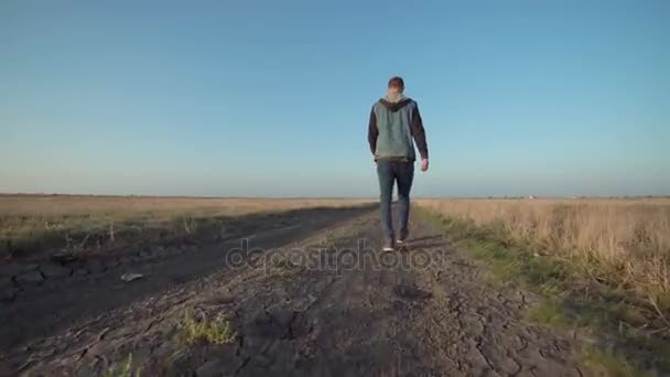 Молодой человек уходит по сельской дороге — стоковое видео