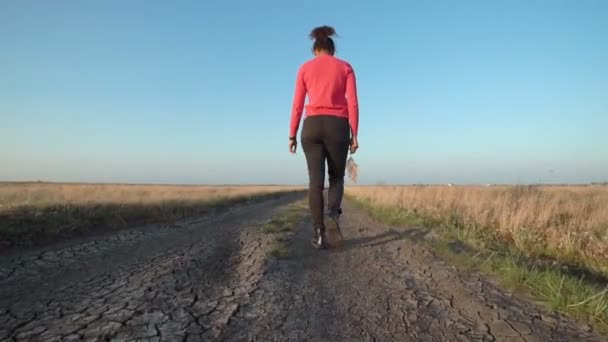 Женщина идет по грунтовой дороге в солнечный день — стоковое видео