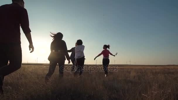 Друзья бегут к ветряной электростанции на закате — стоковое видео