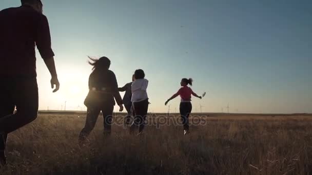 Amigos corriendo hacia el parque eólico al atardecer — Vídeo de stock