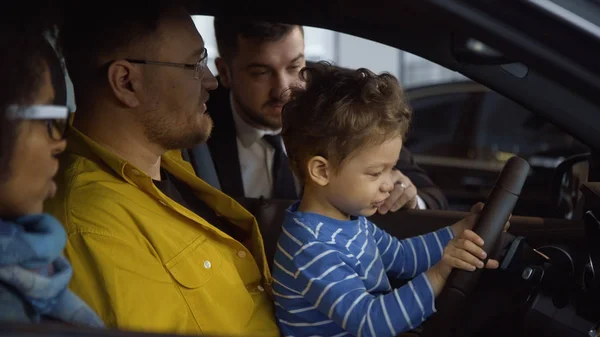 Happy family consulting with dealer in car shop — Stock Photo, Image