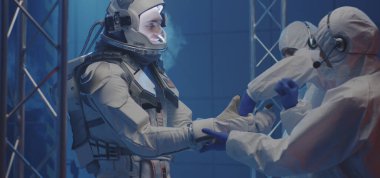 Bilim adamı astronotların eldiven giymesine yardım ediyor.