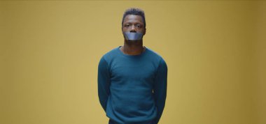 Ağzı bantlı bir adam kameraya bakıyor.