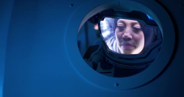 Astronauta femenina mirando desde el ojo de buey de la nave espacial — Vídeos de Stock