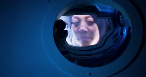 Astronauta femenina mirando desde el ojo de buey de la nave espacial — Vídeo de stock