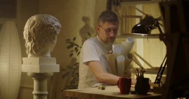 Artista con rollos de papel sentado en el escritorio — Vídeo de stock