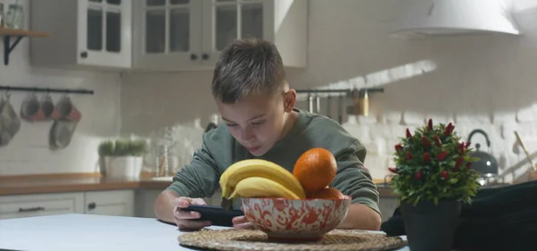 Jongen speelt op zijn smartphone in de keuken — Stockfoto