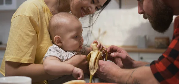 Jovem casal alimentando bebê com banana — Fotografia de Stock