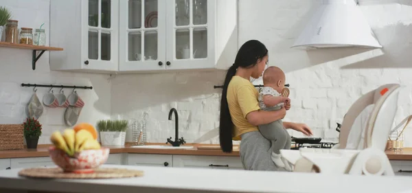 Young mother doing housework while holding baby — Stockfoto