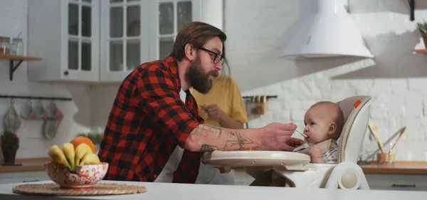 Casal jovem alimentando seu bebê na cozinha — Fotografia de Stock