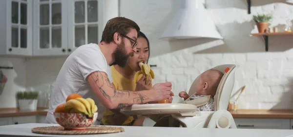 Casal jovem alimentando seu bebê na cozinha — Fotografia de Stock