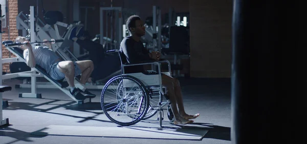 Hombre de silla de ruedas sentado mientras otros hacen ejercicio — Foto de Stock