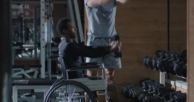 Tekerlekli sandalyedeki adam spor salonunda ağırlık kaldırıyor.