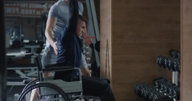 Tekerlekli sandalyedeki adam spor salonunda ağırlık kaldırıyor.