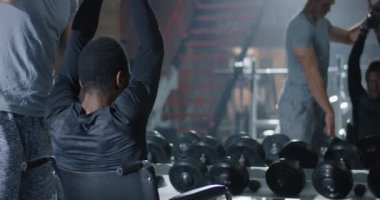 Tekerlekli sandalyedeki adam spor salonunda ağırlık kaldırıyor.