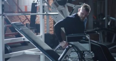 Disabled man moving from wheelchair to training bench