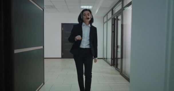 Businesswoman phoning with headset in office corridor — Stock Video