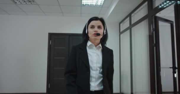 Businesswoman phoning with headset in office corridor — Stock Video