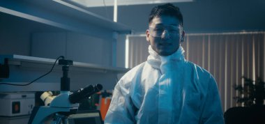 Bilim adamı laboratuvarda kameraya bakıyor.