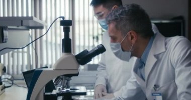 Bilim adamı laboratuvarda kameraya bakıyor.