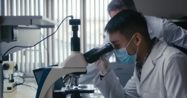Wetenschapper die steekproef in microscoop bestudeert — Stockvideo