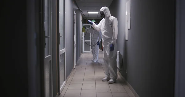 Hombres con trajes de materiales peligrosos desinfectando el edificio —  Fotos de Stock