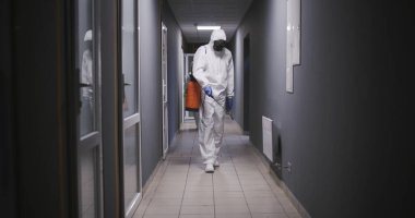 Tehlikeli madde giysileri içindeki adamlar binayı dezenfekte ediyor.