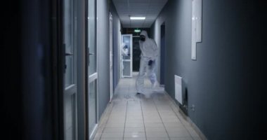 Tehlikeli madde giysisi giymiş adamlar koridorda koşuyor.