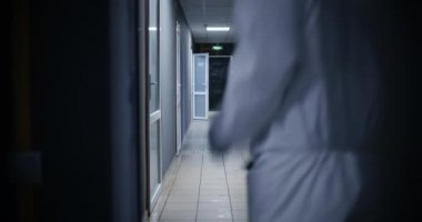 Tehlikeli madde giysisi giymiş adamlar koridorda koşuyor.