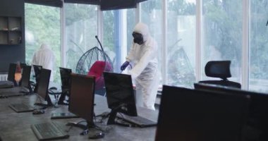 Tehlikeli madde giysileri içindeki adamlar ofisi dezenfekte ediyor.