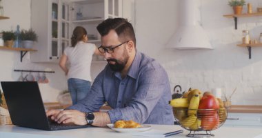 Adam mutfakta dizüstü bilgisayarıyla çalışıyor.